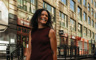 Woman standing on a city street with a building in the background wearing the Birdie & Claire Jordan Dress in burgundy.