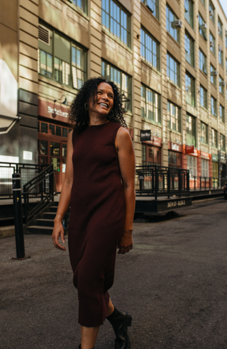 Woman walking on a city street with a building in the background wearing the Birdie & Claire Jordan Dress in burgundy.