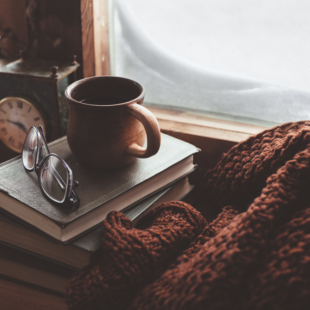 Coffee cup, blanket, and books next to a snow covered window